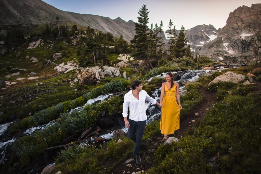 An engaged couple walks next to a waterfall in the Rock Mountains.