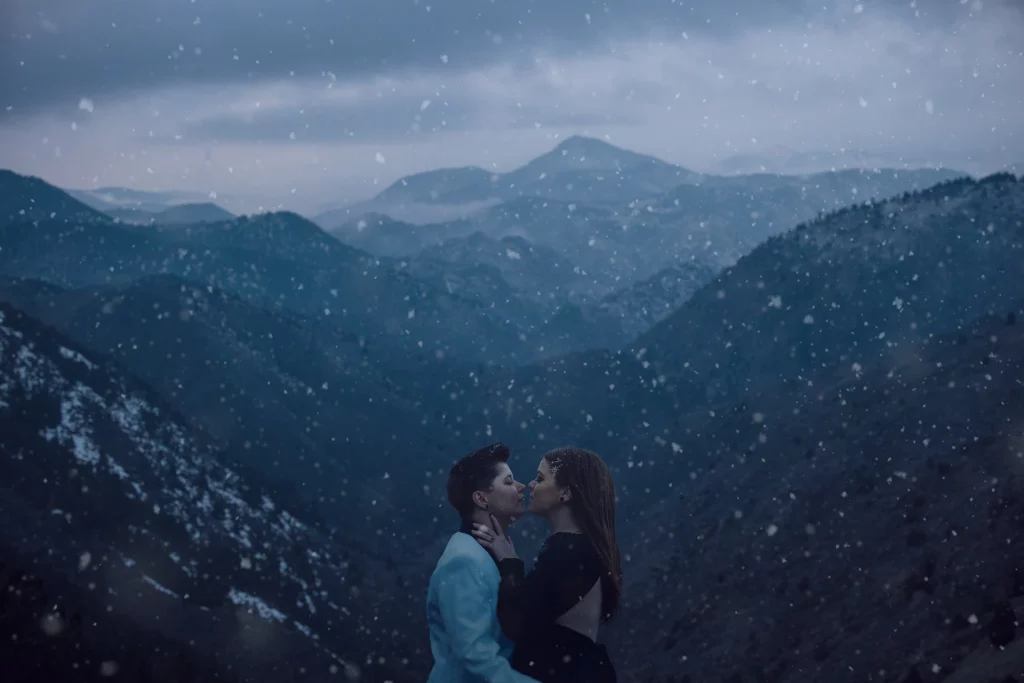 Brides embrace for a kiss in the snow in front of mountains in Golden, CO.