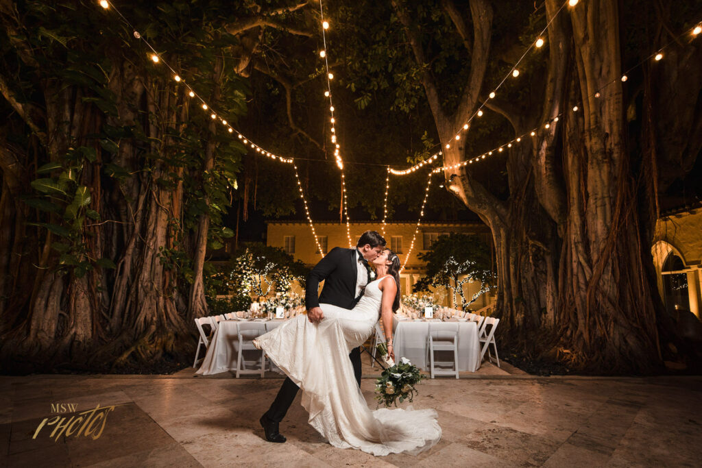 Wedding couple kissing in front of giant banyan trees in at their Boca Raton wedding venue.