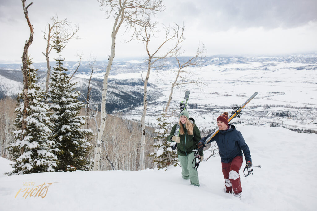 Engaged Colorado couple hiking up a mountain to ski down in Steamboat Springs, CO.