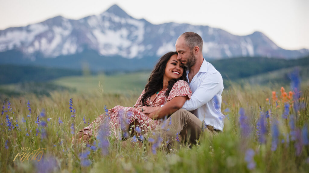 An engaged Colorado couple snuggles in a flowering meadow in Telluride, CO.